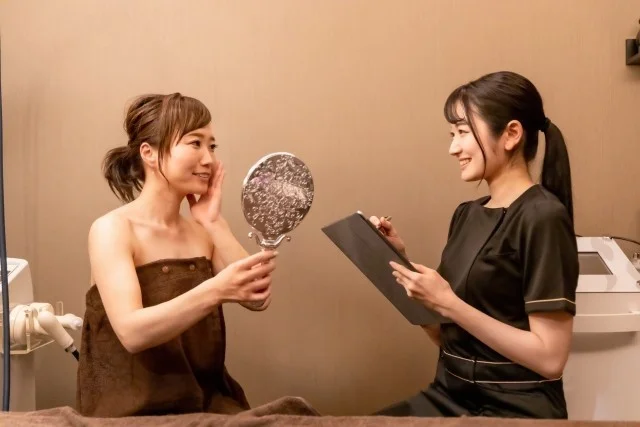 鏡で肌を確認する女性とエステティシャン