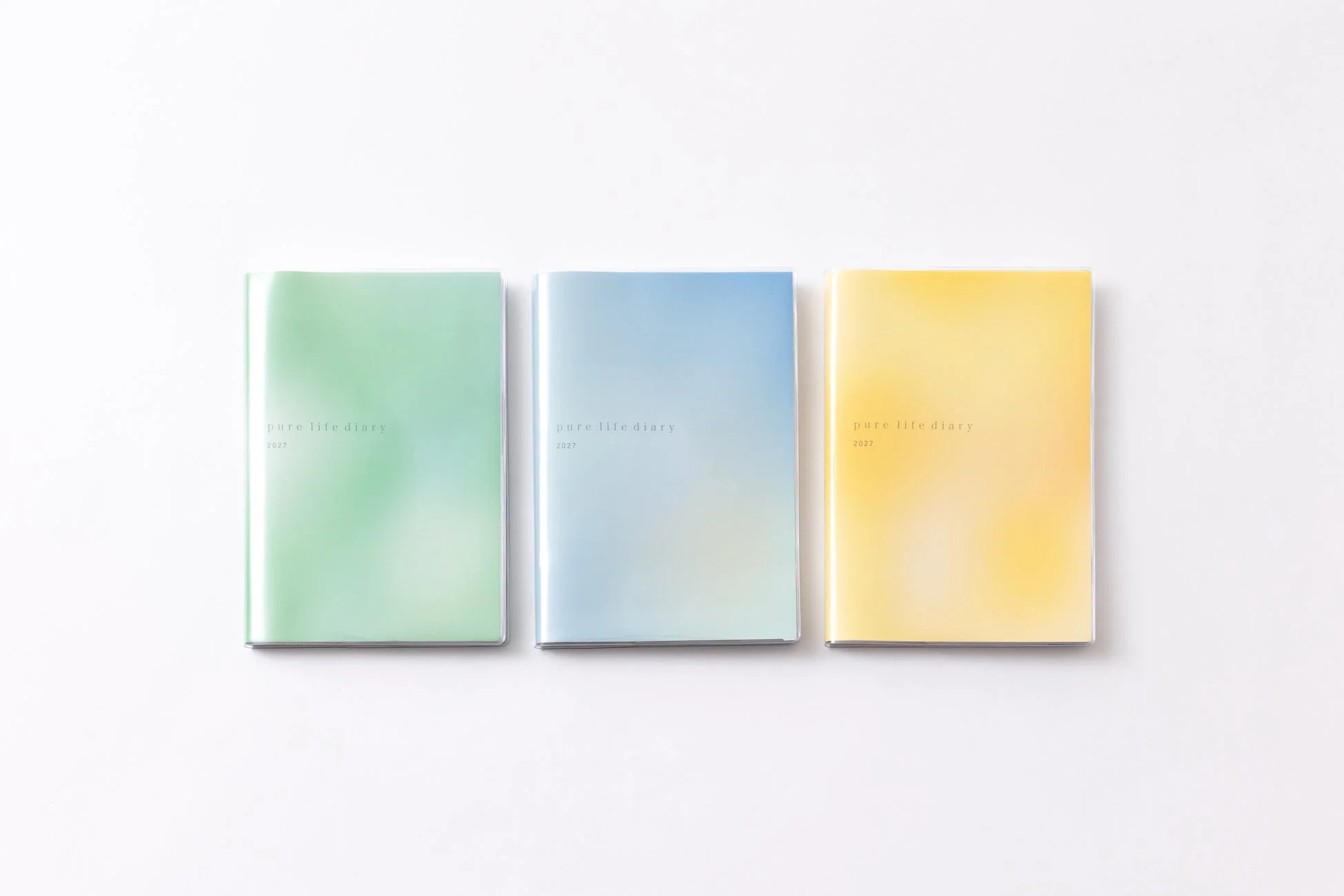 「pure life diary 2027」と書かれた、緑、青、黄色のパステルカラーのグラデーションが美しい3冊の手帳が並べられています。シンプルで清潔感のあるデザインです。