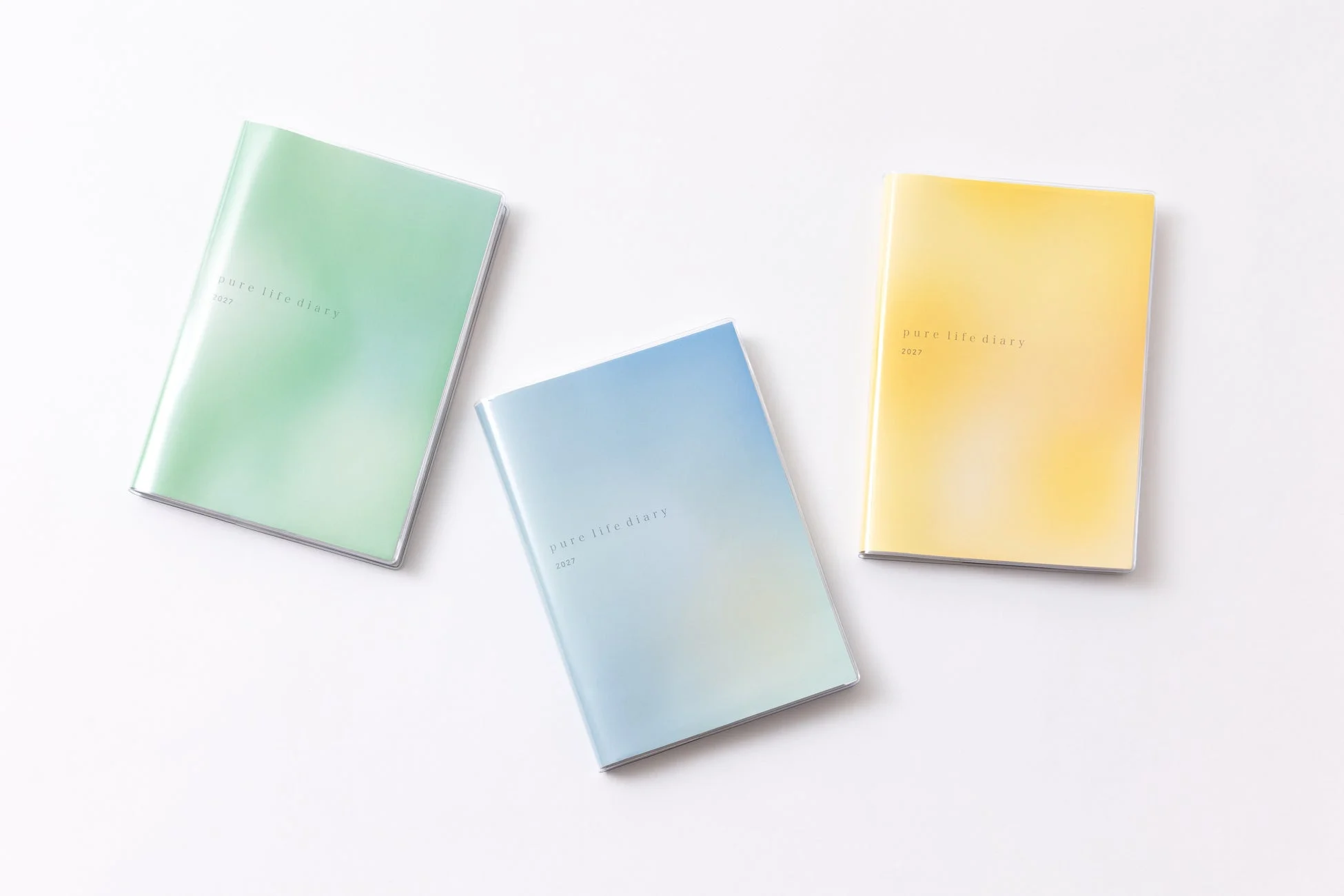 白背景に、ミントグリーン、スカイブルー、レモンイエローのパステルカラーのグラデーションが施された「pure life diary 2027」と書かれた3冊の手帳が並べられています。