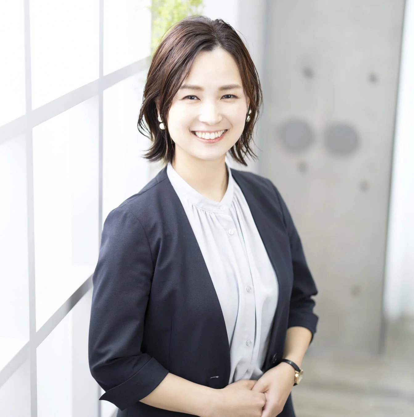 明るい室内で紺色のジャケットを着用した日本人女性が、笑顔でカメラを見つめているポートレート